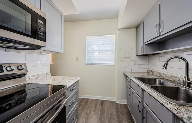 kitchen featuring tasteful backsplash, gray cabinetry, appliances with stainless steel finishes, and dark wood-type flooring