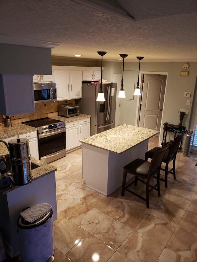 kitchen with light tile patterned flooring, backsplash, decorative light fixtures, appliances with stainless steel finishes, and white cabinetry