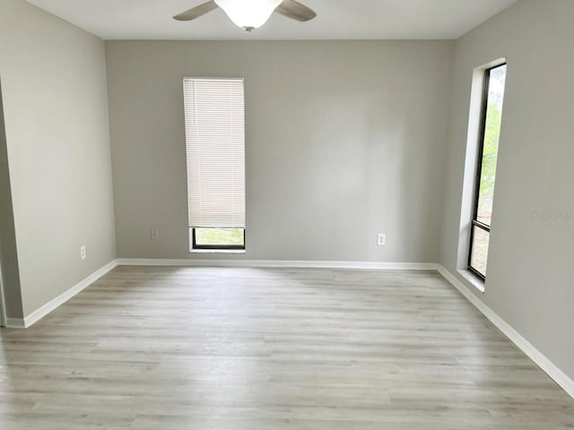 empty room with a wealth of natural light, light wood-style flooring, baseboards, and a ceiling fan