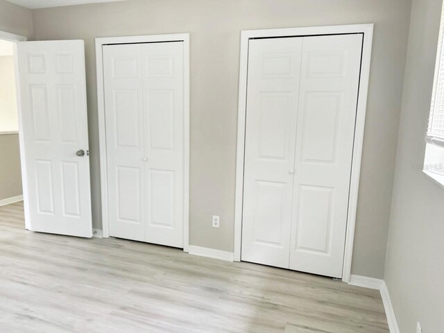 unfurnished bedroom with two closets and light wood-type flooring