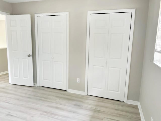 unfurnished bedroom with light wood-style flooring, two closets, and baseboards