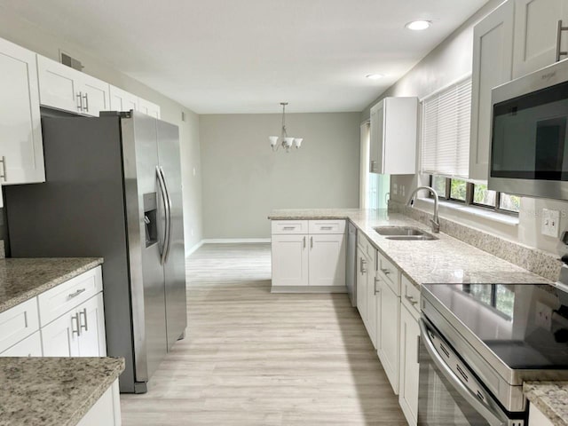 kitchen featuring light stone countertops, stainless steel appliances, a notable chandelier, white cabinetry, and a sink