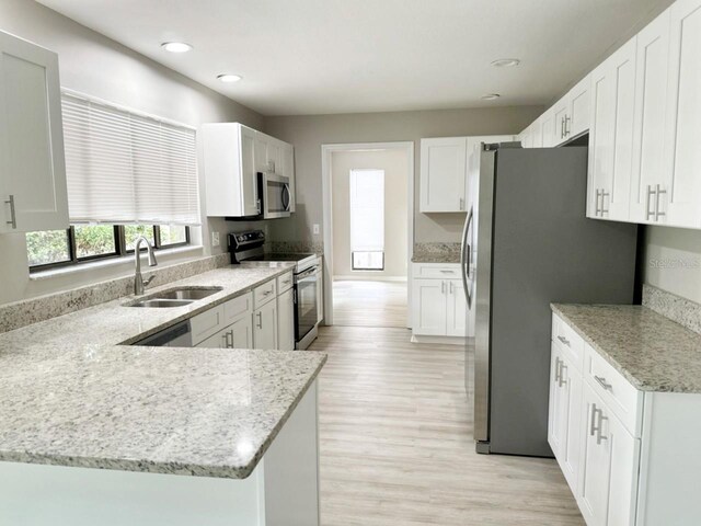 kitchen featuring appliances with stainless steel finishes, light hardwood / wood-style floors, white cabinetry, sink, and light stone counters