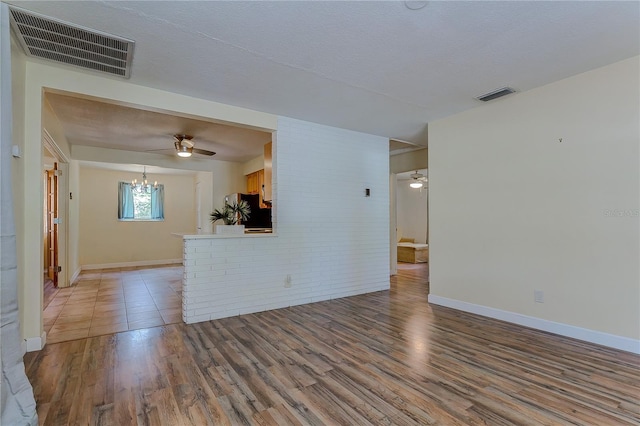 unfurnished living room with hardwood / wood-style flooring, a textured ceiling, and ceiling fan with notable chandelier