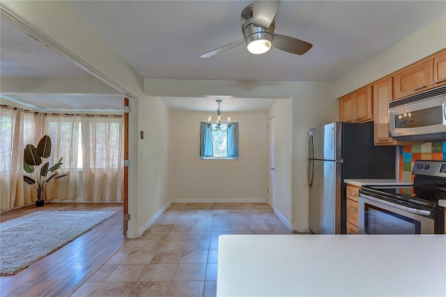 kitchen featuring light tile patterned floors, appliances with stainless steel finishes, ceiling fan with notable chandelier, and pendant lighting