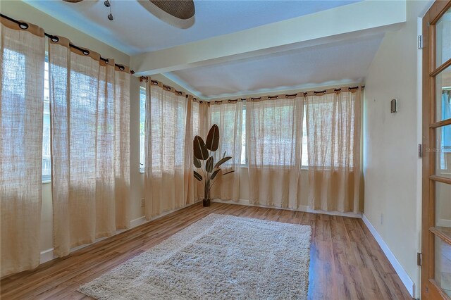 spare room with ceiling fan, light hardwood / wood-style floors, and beamed ceiling