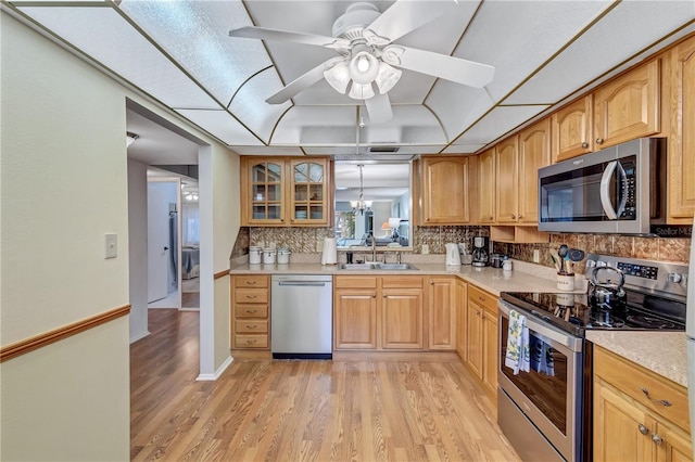 kitchen with appliances with stainless steel finishes, light hardwood / wood-style floors, sink, and backsplash