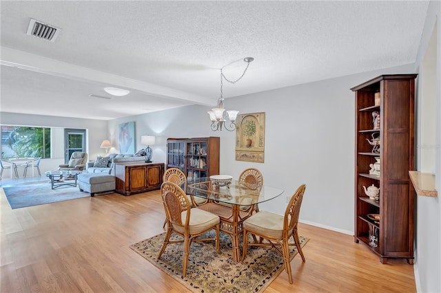 dining area with beam ceiling, an inviting chandelier, light hardwood / wood-style flooring, and a textured ceiling