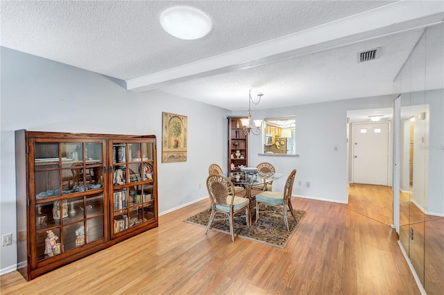 dining room featuring a textured ceiling, beamed ceiling, and light hardwood / wood-style floors