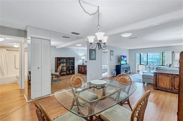 dining space featuring beam ceiling, a notable chandelier, light hardwood / wood-style flooring, and a textured ceiling