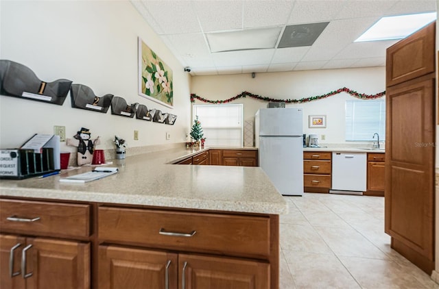 kitchen with white appliances, brown cabinetry, a sink, and a paneled ceiling