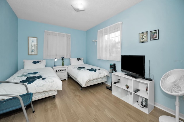 bedroom with a textured ceiling, wood finished floors, and baseboards