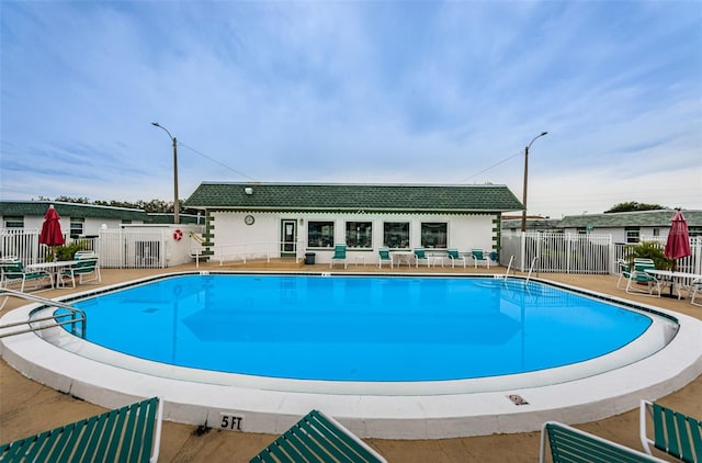 pool with fence, an outdoor structure, and a patio