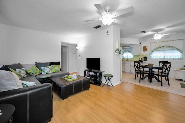 living area with a ceiling fan, light wood-style flooring, visible vents, and a textured ceiling