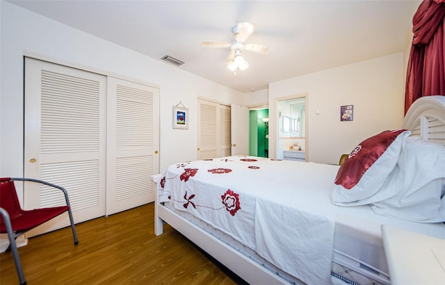 bedroom with two closets, ceiling fan, visible vents, and wood finished floors