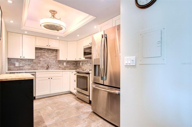 kitchen with appliances with stainless steel finishes, white cabinetry, a raised ceiling, and backsplash