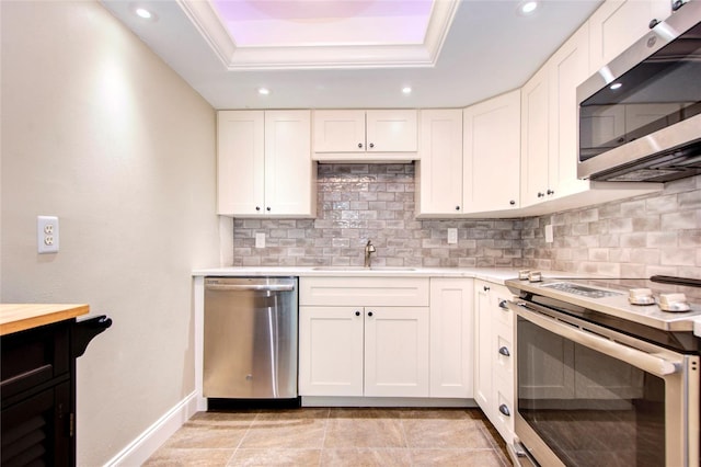 kitchen with stainless steel appliances, a sink, light countertops, a tray ceiling, and tasteful backsplash