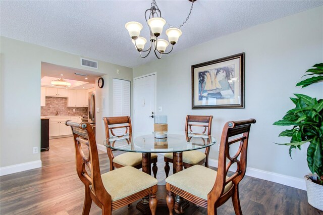 dining space with a textured ceiling, an inviting chandelier, and dark hardwood / wood-style flooring