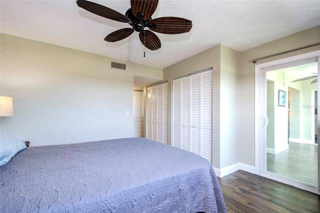 bedroom with a textured ceiling, ceiling fan, dark hardwood / wood-style floors, and multiple closets