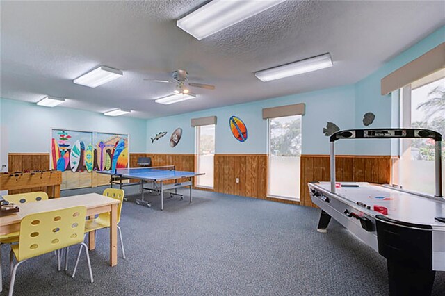 playroom with a textured ceiling, carpet, ceiling fan, and wood walls