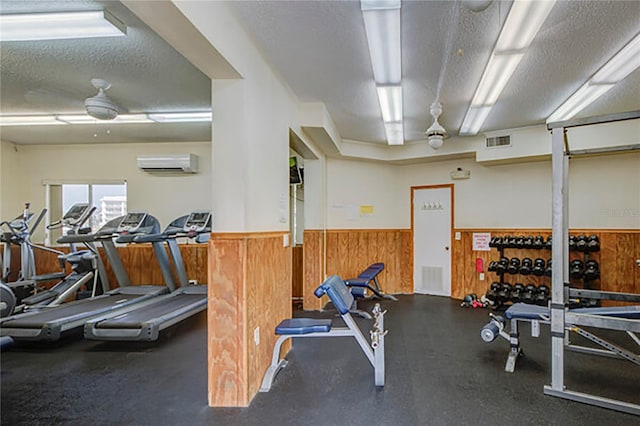 gym with a textured ceiling, an AC wall unit, wood walls, and ceiling fan