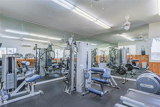 exercise room with a ceiling fan, a wainscoted wall, a textured ceiling, wood walls, and a wall mounted AC