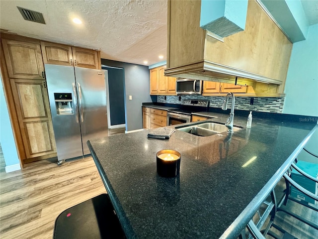 kitchen with sink, light hardwood / wood-style floors, tasteful backsplash, a textured ceiling, and stainless steel appliances