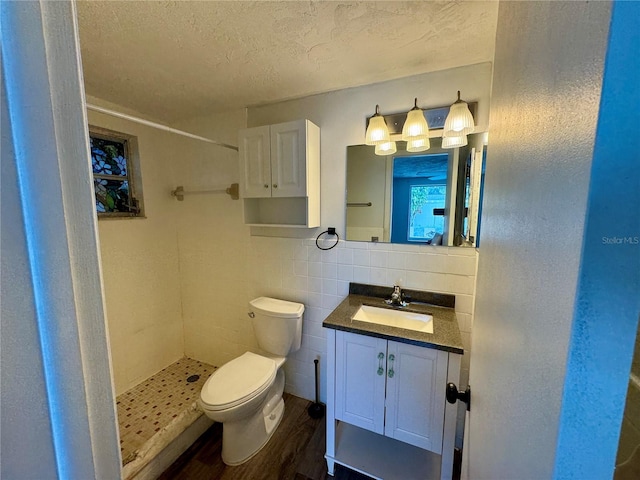 bathroom with vanity, a textured ceiling, a tile shower, tile walls, and toilet