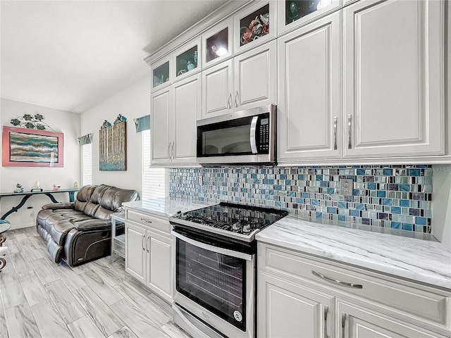 kitchen with tasteful backsplash, light stone countertops, stainless steel appliances, and white cabinetry