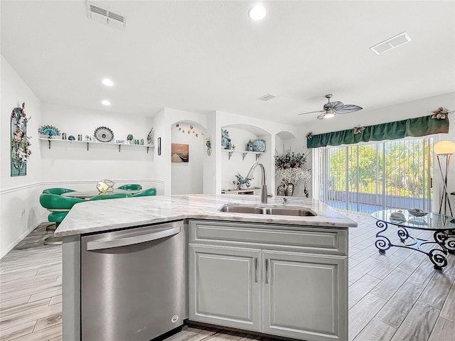 kitchen with ceiling fan, stainless steel dishwasher, sink, a kitchen island with sink, and light stone counters