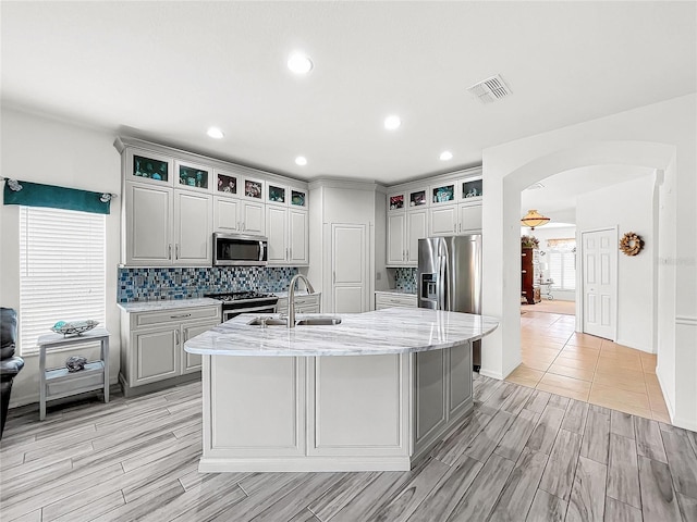 kitchen with decorative backsplash, sink, appliances with stainless steel finishes, an island with sink, and light stone counters