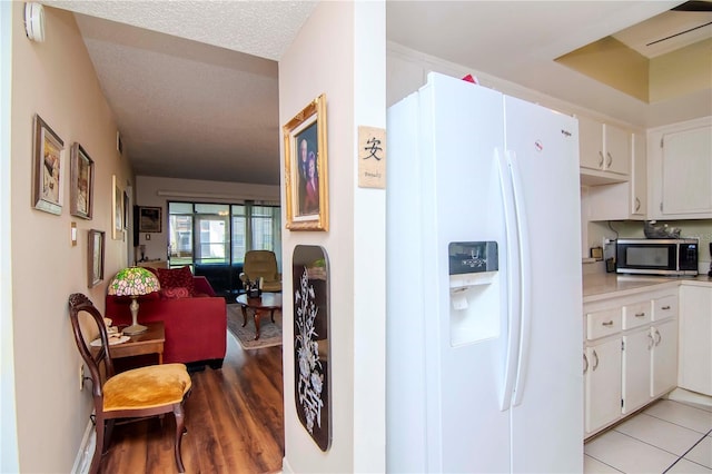 kitchen with white cabinetry, light tile patterned flooring, white fridge with ice dispenser, and a textured ceiling