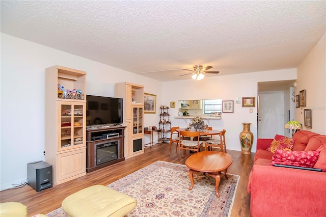 living room with hardwood / wood-style flooring, ceiling fan, and a textured ceiling