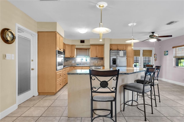 kitchen with light tile patterned flooring, appliances with stainless steel finishes, tasteful backsplash, a kitchen island, and ceiling fan