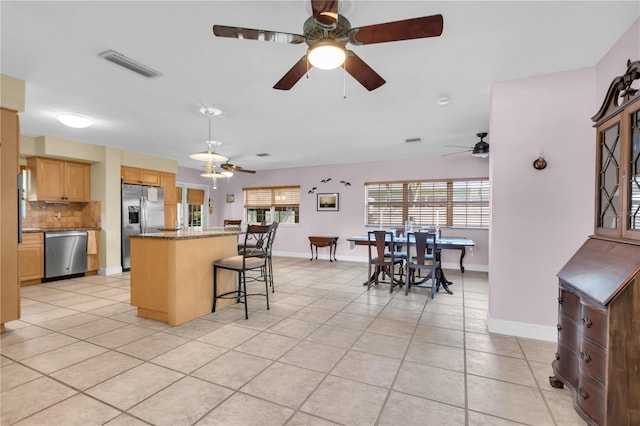 kitchen with ceiling fan, a kitchen breakfast bar, backsplash, appliances with stainless steel finishes, and light tile patterned floors