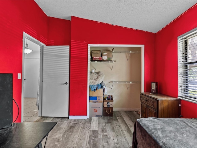 bedroom featuring vaulted ceiling, light hardwood / wood-style flooring, a closet, and a textured ceiling