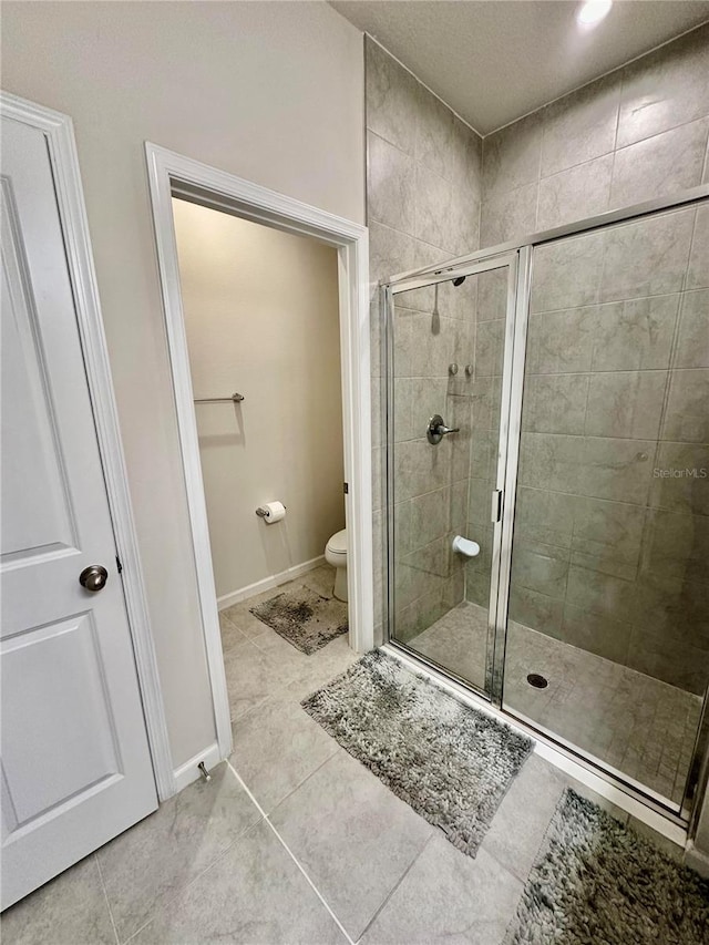 bathroom with tile patterned floors, toilet, and a shower with door