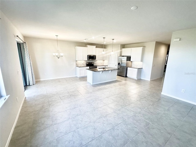 kitchen with a kitchen island with sink, an inviting chandelier, decorative backsplash, white cabinetry, and stainless steel appliances