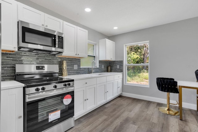 kitchen featuring light hardwood / wood-style flooring, sink, white cabinetry, stainless steel appliances, and decorative backsplash