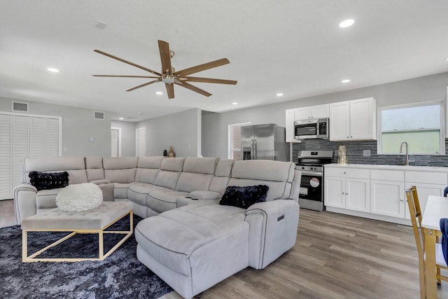 living room with ceiling fan, sink, and light wood-type flooring