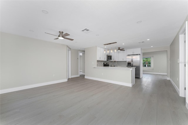 unfurnished living room with visible vents, baseboards, ceiling fan, light wood-style flooring, and a sink