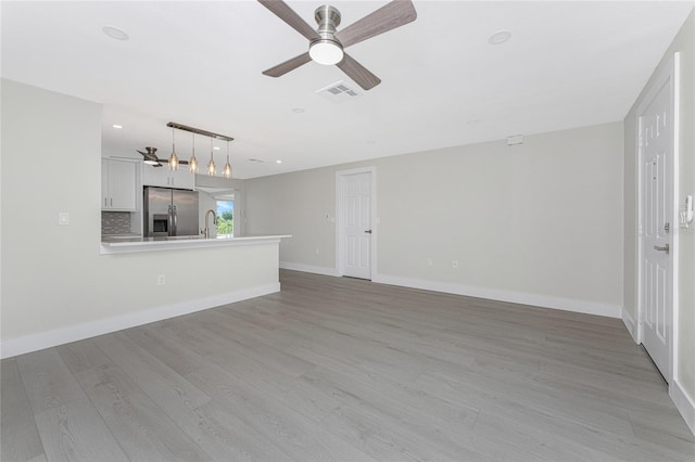 unfurnished living room with visible vents, a sink, light wood finished floors, baseboards, and ceiling fan