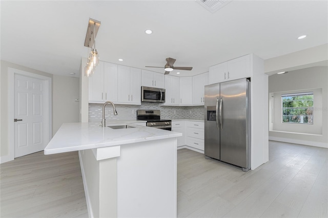 kitchen with visible vents, a sink, appliances with stainless steel finishes, a peninsula, and decorative backsplash