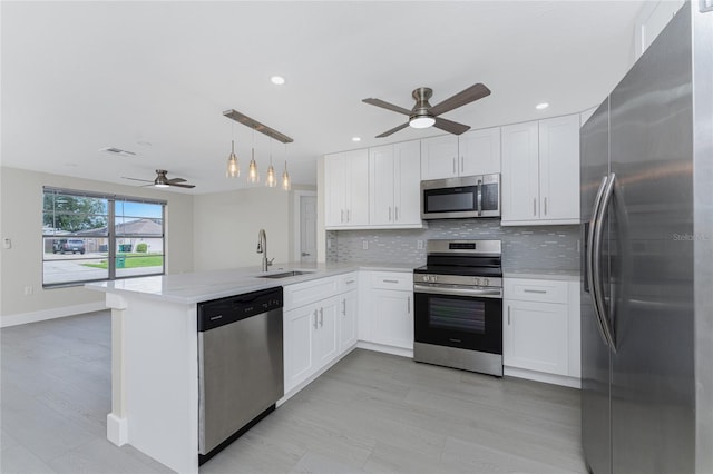 kitchen with a peninsula, a sink, stainless steel appliances, white cabinetry, and tasteful backsplash