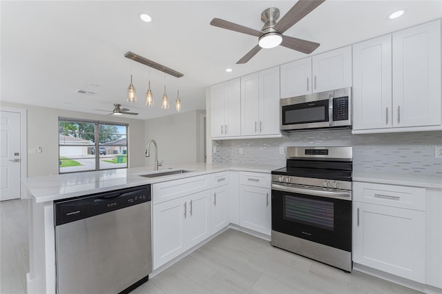 kitchen with a sink, backsplash, white cabinetry, appliances with stainless steel finishes, and a peninsula