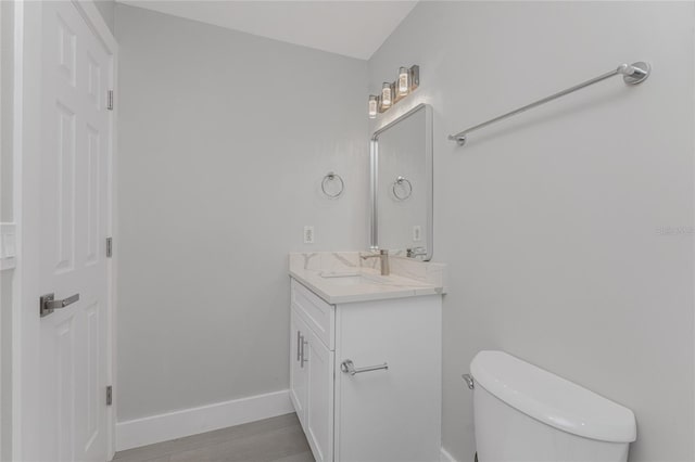 half bath featuring toilet, vanity, baseboards, and wood finished floors