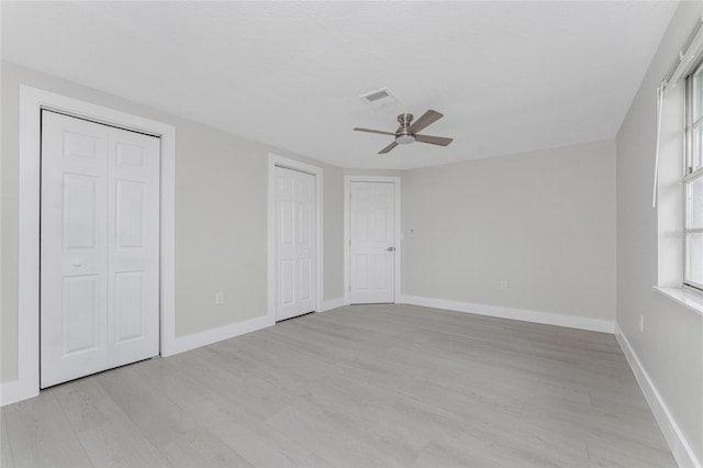 unfurnished bedroom featuring light wood-style floors, baseboards, two closets, and visible vents