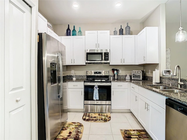 kitchen featuring sink, dark stone countertops, appliances with stainless steel finishes, light tile patterned floors, and white cabinets