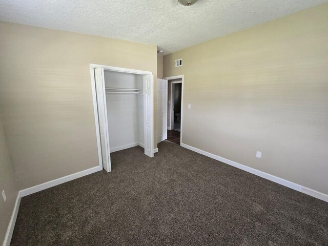 unfurnished bedroom featuring a closet, a textured ceiling, and dark carpet