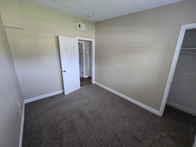 unfurnished bedroom with a textured ceiling, a closet, and dark carpet